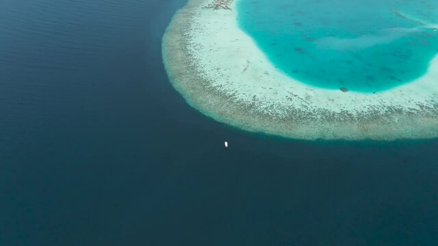 Large boat approaches huse coral reef in The Maldives with stunning colours