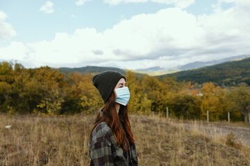 Portrait of a woman in a medical mask on a meadow in the mountains autumn dry grass