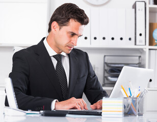 Serious businessman sitting at table and working on laptop in office