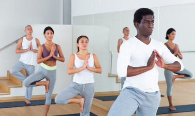 Multiethnic group of young sporty people practicing yoga, standing together in asana