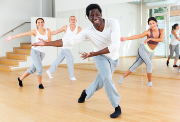 Fototapeta na wymiar Portrait of emotional young adult man doing exercises during group class in dance center