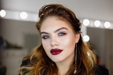 Young woman with bright makeup in dressing or makeup room near mirror. Make up process. Making mua...