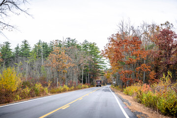 Dark red big rig tip semi truck with dump trailer running on the forest road with autumn trees on the side