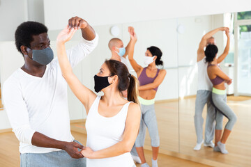 Young Hispanic woman and African American man in protective face masks learning to dance waltz...