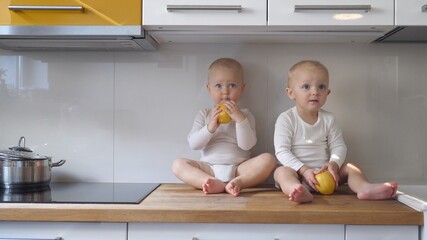 Two twin baby girls play on kitchen table top with lemons patiently waiting for food to be cooked....