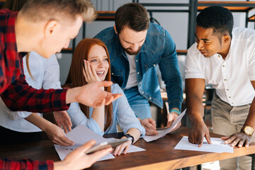 Close-up of exhausted overworked young business woman under stress at office. Colleagues shaking paper documents on blurry background. Business team wants to get answer and decision from boss.