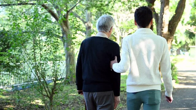 高齢の父を労わって散歩道を歩く息子