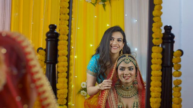 Beautiful sister putting Chunni/veil on a cheerful bride's head - the bridal look . Medium shot of an Indian Punjabi bride smiling and getting ready for her Indian marriage - wedding rituals