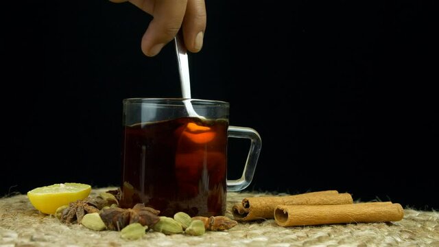 Preparing a cup of green tea with different Indian spices 

. Closeup shot of a person's hand stirring green tea surrounded by lemon  cinnamon  cardamom  and star anise spices 