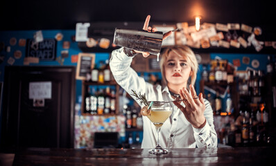 Charismatic girl barman formulates a cocktail while standing near the bar counter in pub
