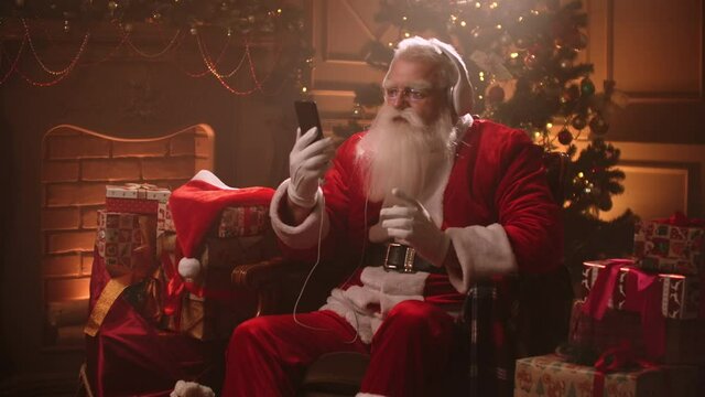 happy Xmas holidays of Santa Claus, old wizard is sitting in house and listening to song by headphones