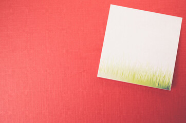 White blank memo with grass on a red textured surface