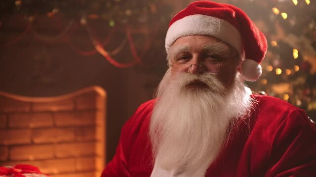 friendly Santa Claus is saying ho-ho-ho sitting in living room at Christmas evening, portrait of wizard 