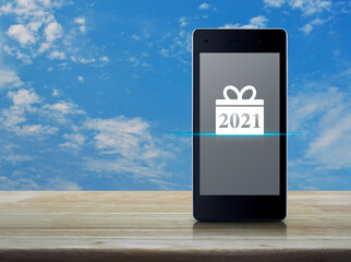 Gift box happy new year 2021 flat icon on modern smart mobile phone screen on wooden table over blue sky with white clouds, Business happy new year 2021 shop online concept