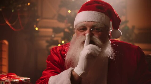 mysterious atmosphere of Christmas night, portrait of Santa Claus in room with decorations, wizard is asking hush by finger gesture