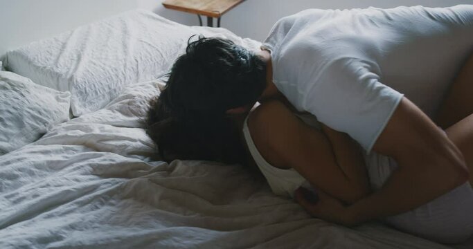 Cinematic close up shot of young just married couple wearing pajamas having fun to tickling each other on the bed in the bedroom just woke up early in the morning in a sunny day.
