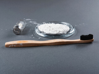 Zero waste concept for teeth cleaning. A bamboo toothbrush with a floss in a glass and toothpowder on the grey background.