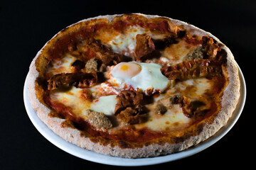 Pizza with egg in the middle, sausages and bacon. Low key background. Traditional Italian pizza