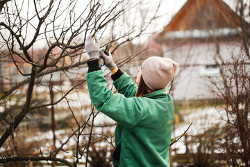 Caucasian cute woman gardener with garden tool close up, gardener pruning branches with pruning shears, winter plant pruning, winter gardening work in winter work clothes