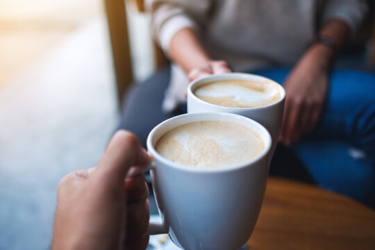 Closeup image of man and woman clinking white coffee mugs in cafe