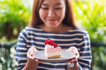 Closeup image of a beautiful young asian woman holding a piece of strawberry cheese cake in a plate