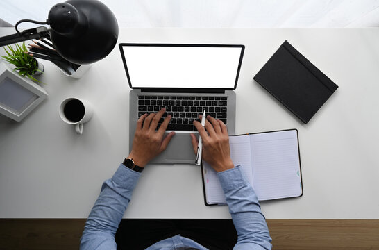 Top view of man is working on laptop while sitting at the white wooden desk.