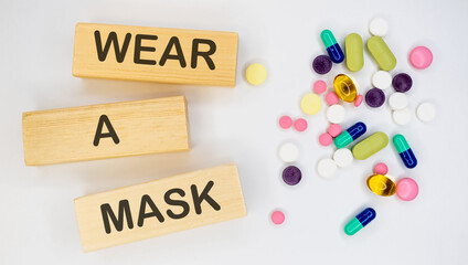WEAR A MASK is on long wooden blocks on a white background with pills. Medical concept.