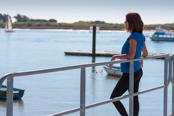 beautiful young girl leaning on the railing of a pier looking to the horizon