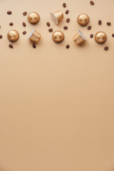Fototapeta premium Caffeine, hot drinks and objects concept - close up of golden capsules or pods for coffee mashine with some roasted grains on beige background. Top view with space for text. Flat lay..