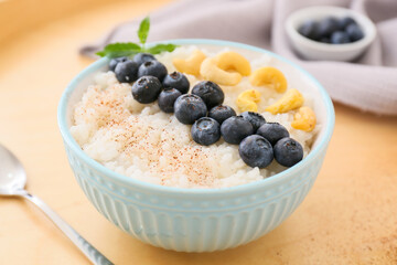 Bowl of tasty rice pudding with blueberry and cashew on wooden tray