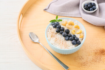 Bowl of tasty rice pudding with blueberry and cashew on wooden tray