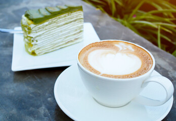 Latte or cappuccino coffee in white cup with green tea cake on table