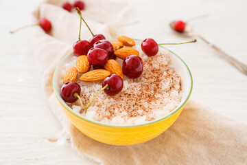 Bowl of tasty rice pudding with cherry and nuts on light table