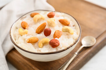 Bowl of tasty rice pudding with nuts on wooden board
