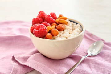 Bowl of tasty rice pudding with raspberry and nuts on napkin