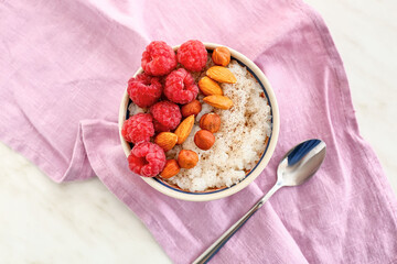 Bowl of tasty rice pudding with raspberry and nuts on napkin