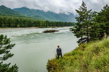 Woman admiring the rapid flow of a mountain river on the background of mountains covered with clouds