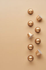 Caffeine, hot drinks and objects concept - close up of golden capsules or pods for coffee mashine on beige background. Top view with space for text. Flat lay..