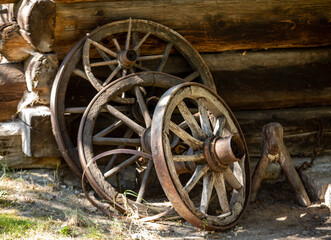 Fototapeta na wymiar Wooden wheels from an ancient cart standing in front of the wall of a wooden country cottage