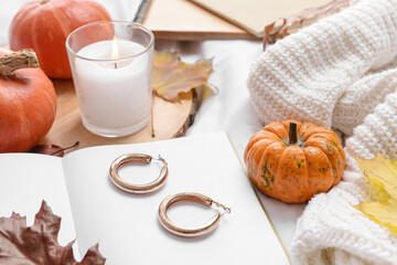 Beautiful autumn composition with book, female jewelry and aroma candle on bed