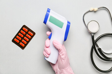 Hand of doctor with infrared thermometer, pills and stethoscope on light background