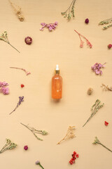 Fototapeta na wymiar Top view of face serum bottle with pipette on beige background. Dried multicolored flowers around bottle. Alternative medicine, herbal essence, sustainable lifestyle concept. Flat lay.
