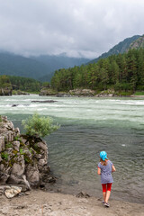 Girl on the river bank against the mountains and cloudy sky