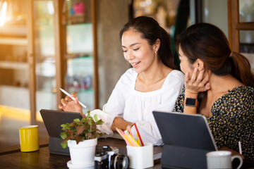 Two beautiful Asian women Sitting at work online or studying during the corona virus with a tablet in the morning, the sun warms happily.