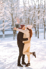 Fototapeta na wymiar Happy couple hugging and kissing outdoors in winter park. Young man and woman enjoy each other in snow forest. Holidays, season, love and leisure concept.