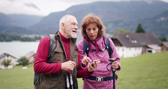 Senior pensioner couple hikers with smartphone in nature, using map for orientation.
