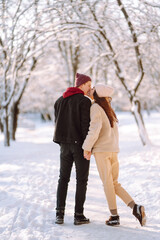 Fototapeta na wymiar Happy couple hugging and kissing outdoors in winter park. Young man and woman enjoy each other in snow forest. Holidays, season, love and leisure concept.