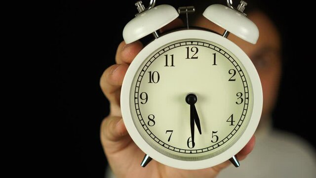 5:30 o'clock. Human hand holding alarm clock that showing five-thirty o'clock and ringing.