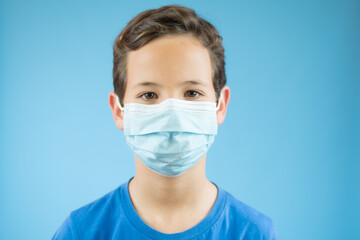 Handsome brunette boy in medical mouth mask over blue background