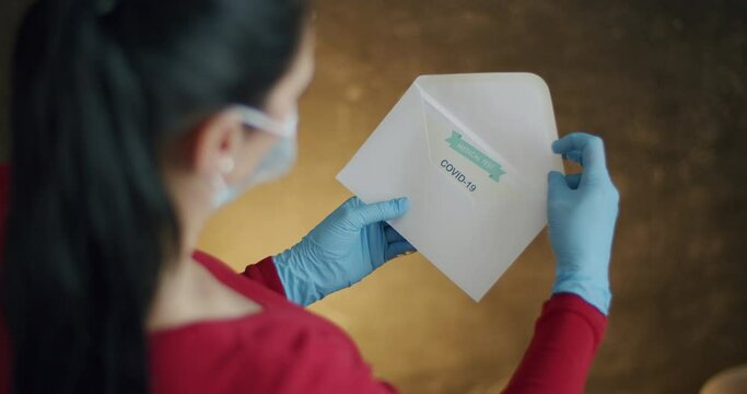 Woman Opening Envelope with Certificate with Negative Results in Covid-19. Over Shoulder View of Woman Wearing Surgical Gloves Opening Envelope and Pulling Out Negative Test Results in Coronavirus.